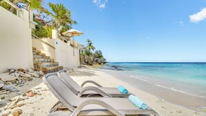 A beach with a lounge chair and umbrella, a staircase leading to a building, and a clear view of the ocean.