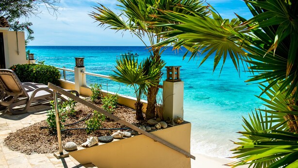 A pool area with a clear view of the ocean, a chair, and a small garden with rocks and plants.