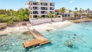 A beachfront hotel with multiple balconies, a pool, and a pier extending into the clear turquoise water.