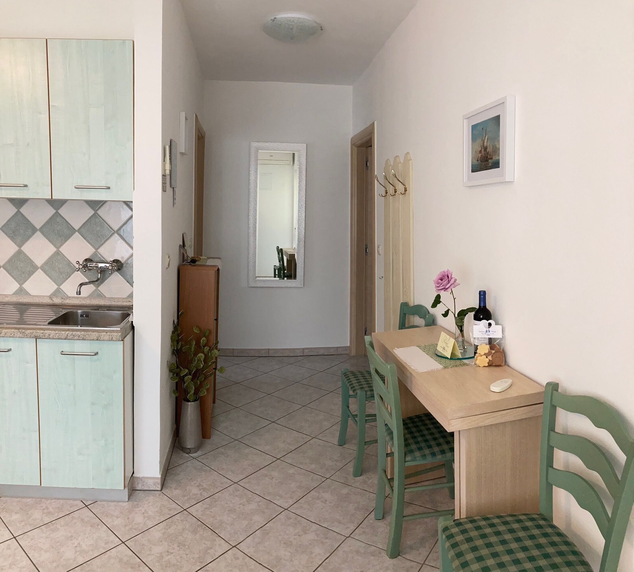 Una cocina compacta con pileta, alacenas y un salpicadero de azulejos. Hay una zona de comedor con una mesa, sillas y un florero con flores.