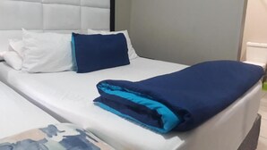 A neatly made bed with white and blue bedding, a headboard, and a plain wall. - Central Sandton Apartment (Sandton)