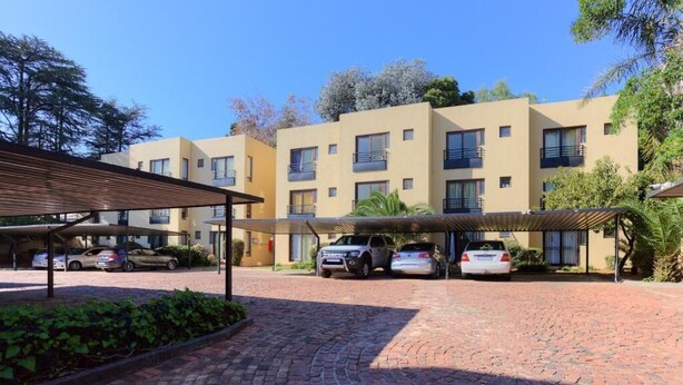 A multi-story building with a covered parking area and a paved walkway. - Central Sandton Apartment (Sandton)
