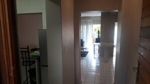 A hallway leading to a dining area with a table and chairs, a refrigerator, and a view of the living room through an open door. - Central Sandton Apartment (Sandton)