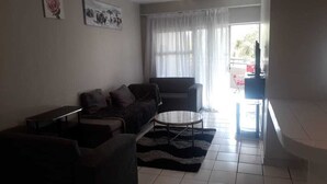 A living room with a sofa, armchair, coffee table, and a TV. - Central Sandton Apartment (Sandton)