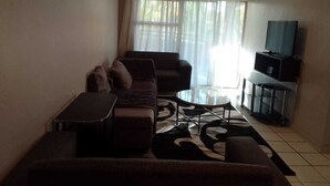 A living room with a sofa set, a coffee table, and a television on a stand. - Central Sandton Apartment (Sandton)