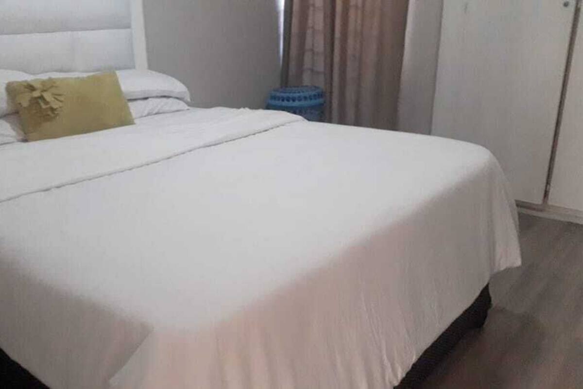 A neatly made bed with white bedding and a single yellow pillow.