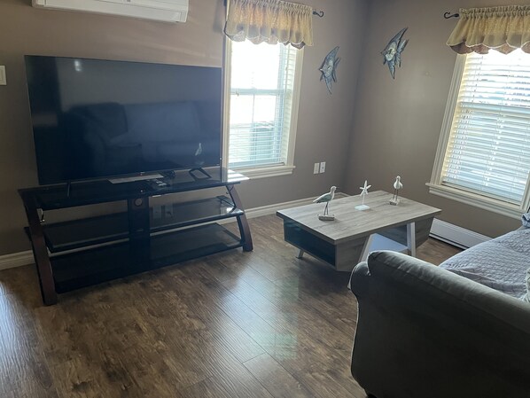 A living room with a flat-screen TV on a glass table, a wooden coffee table, a sofa, and decorative wall art.
