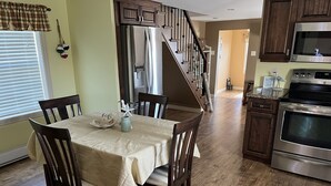 A kitchen with wooden cabinets, a stainless steel refrigerator, a microwave, and an oven. There is a dining table with chairs and a vase with a bird figurine.