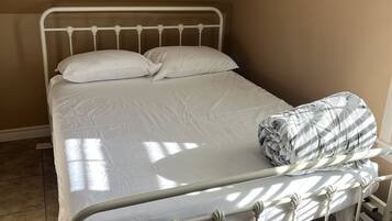 Uma cama de solteiro com estrutura de metal, roupa de cama branca e um edredom listrado.