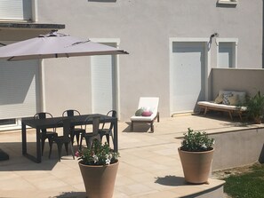 Un patio al aire libre con una mesa, sillas, una tumbona, una planta en maceta y un paraguas grande.