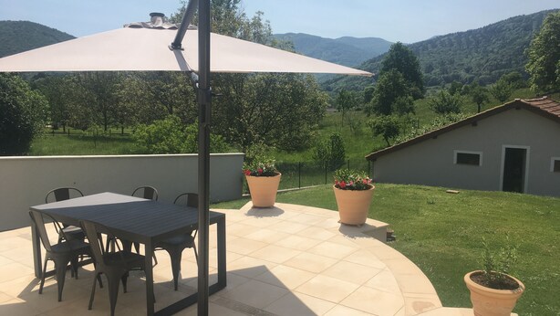 Un patio con mesa y sillas, rodeado de plantas en macetas y un paraguas grande.