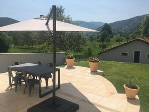 Un patio con mesa y sillas, rodeado de plantas en macetas y un paraguas grande.