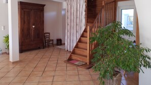 Una habitación amplia con una escalera de madera, un armario grande, una silla, una mesita y una planta en maceta.
