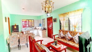 A living room with a sofa, chairs, a dining table, and a kitchen area in the background.