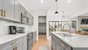 A modern kitchen with grey cabinets, a large island, a built-in microwave, and a stainless steel range hood. - Modern 4 Bed/3.5 Bath Farmhouse Steps to Downtown CF! (Cedar Falls)