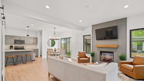 A modern living room with a sofa, two armchairs, a fireplace, and a TV mounted on the wall. - Modern 4 Bed/3.5 Bath Farmhouse Steps to Downtown CF! (Cedar Falls)