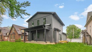 A two-story house with a dark exterior, a front porch, and a well-maintained lawn. - Modern 4 Bed/3.5 Bath Farmhouse Steps to Downtown CF! (Cedar Falls)