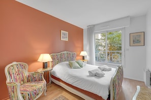 A bedroom with a large bed, two chairs, a nightstand, and a window with a view of trees.