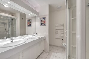 Et moderne badeværelse med to håndvaske, en glasvæg omkring bruseren og et toilet.