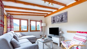 Una sala de estar con un sofá, televisión, techo de madera y ventana con vista a las montañas.