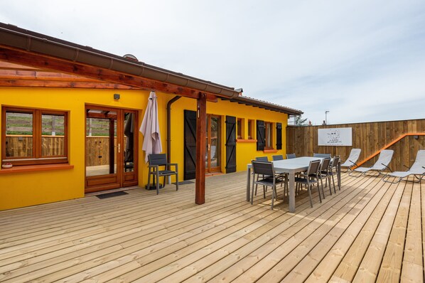Un edificio amarillo con terraza de madera, asientos al aire libre y un cartel.