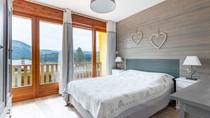 Un dormitorio con una cama grande, suelo de madera, un balcón con vistas y una pared decorada con corazones.