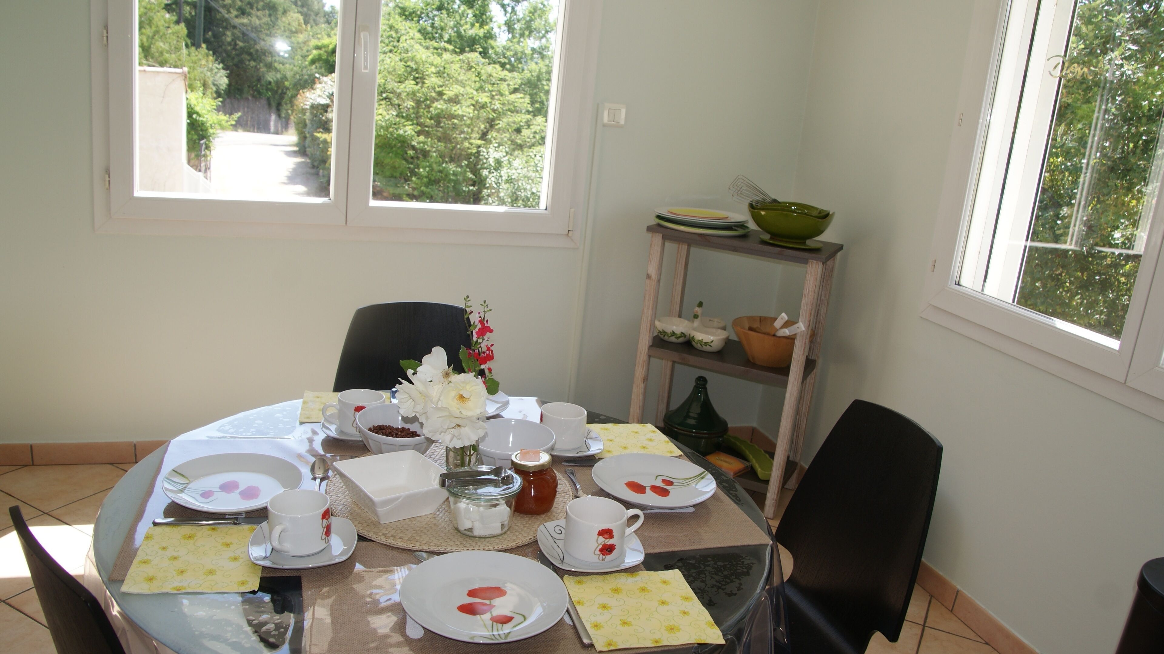 A dining table set with plates, cups, and a vase of flowers, with a window view of greenery.