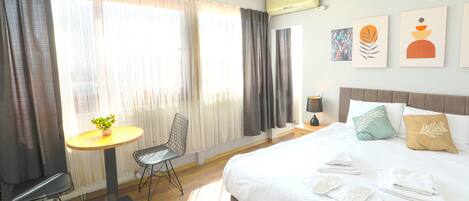 Une chambre d’hôtel avec un lit, une table ronde ornée d’une plante, une chaise et des œuvres d’art accrochées au mur.