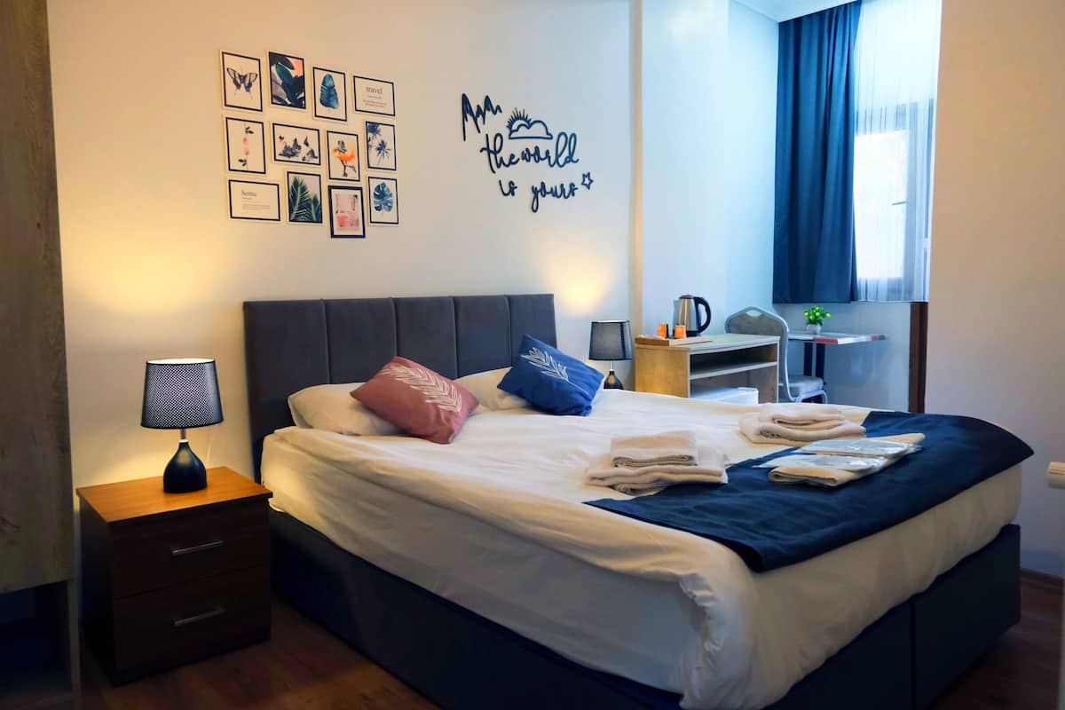 A neatly made bed with pillows, a bedside lamp, and a wall with travel-themed decor.