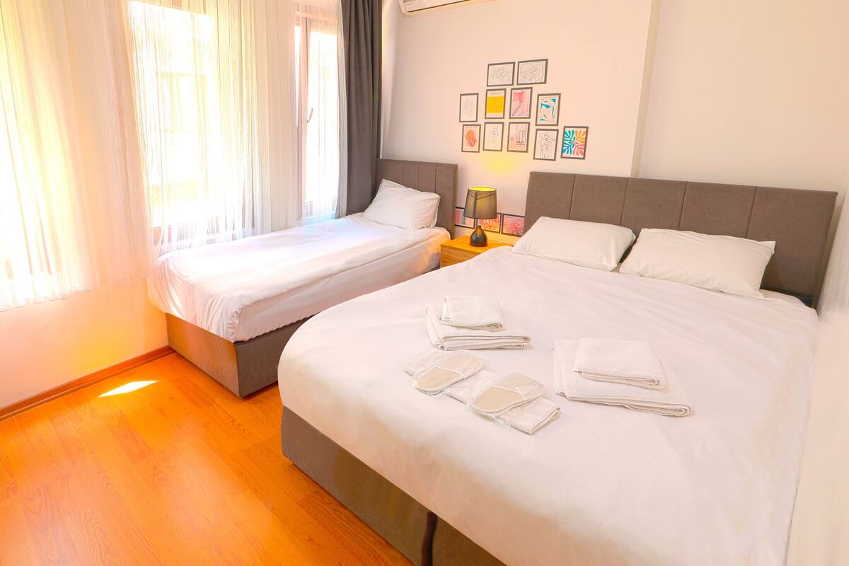 A hotel room with two beds, a nightstand with a lamp, and artwork on the wall.