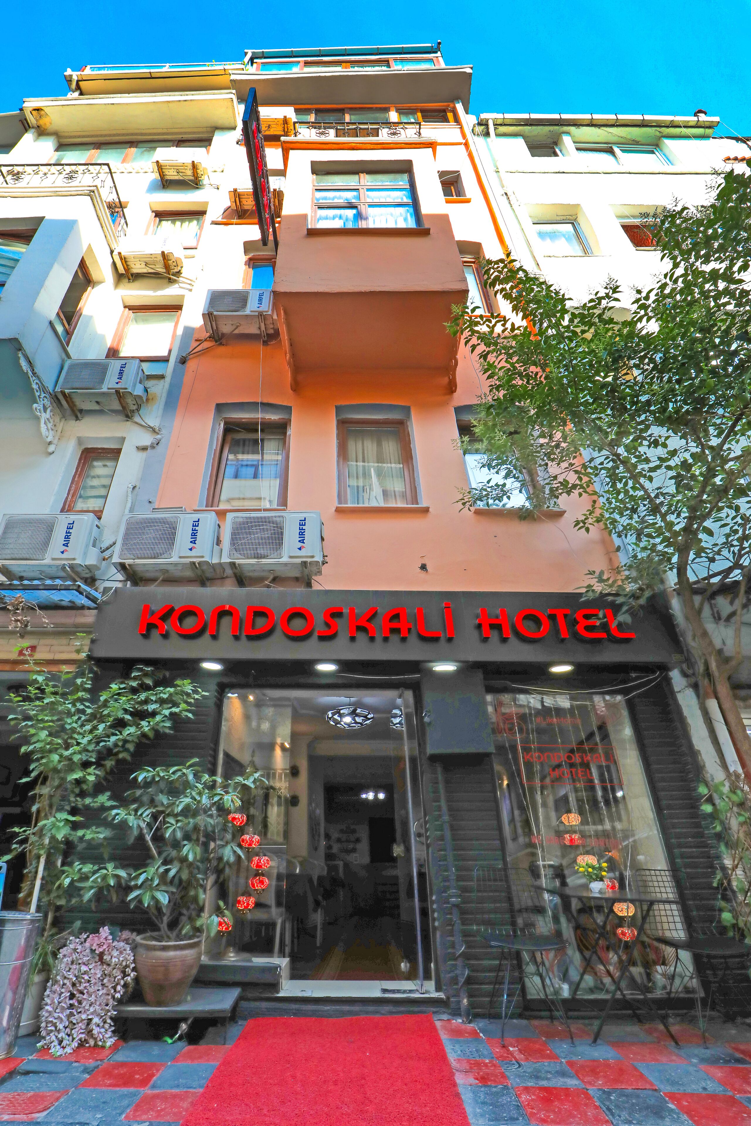 The Kondoskali Hotel entrance with a red carpet, potted plants, and a clear blue sky.