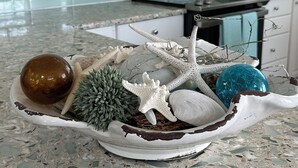 Una cocina con armarios blancos, un microondas y un tazón decorativo con conchas marinas y estrellas de mar sobre una encimera de terrazo.