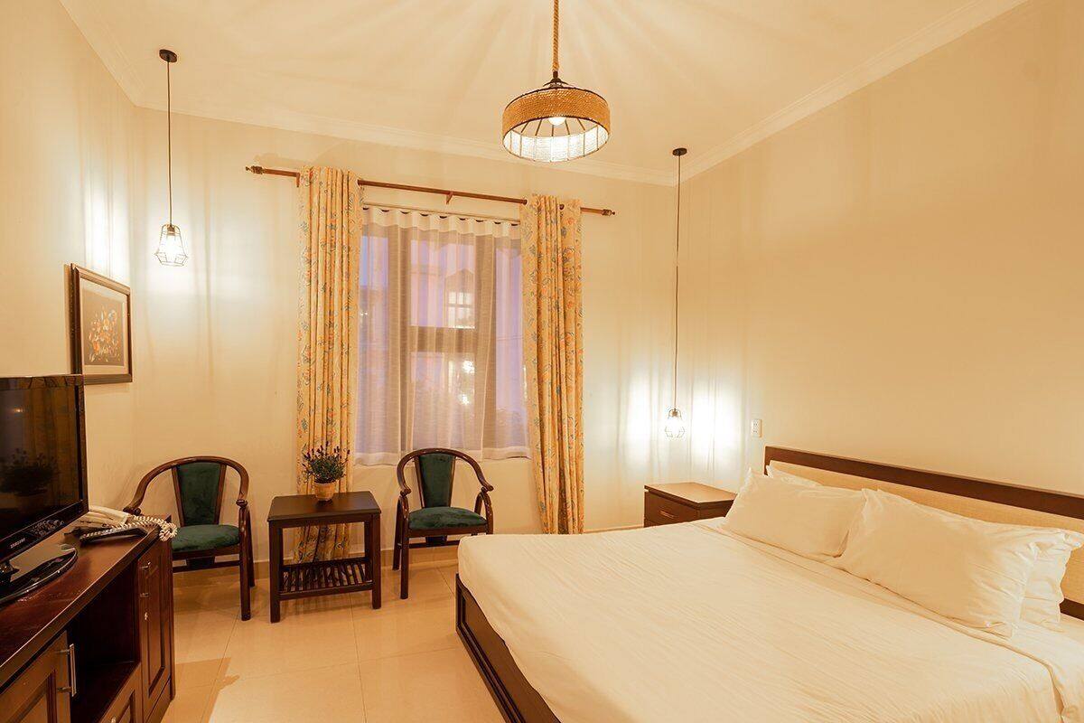 A hotel room with a bed, a desk with a chair, a television, and a window with curtains.