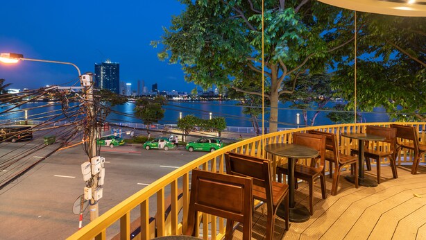 A terrace with wooden furniture and a view of a cityscape at night. - Danapearl Riverside Condotel (Da Nang)