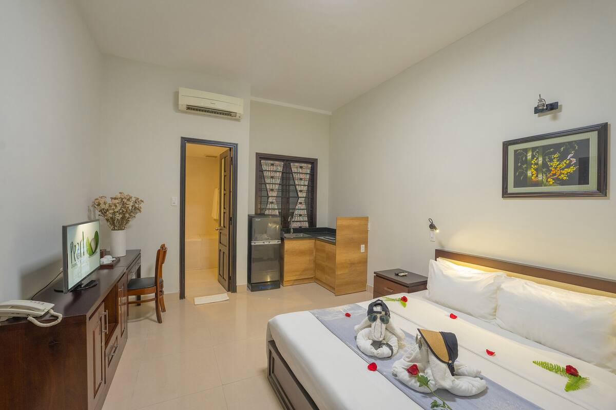 A hotel room with a bed, a desk, a chair, a small kitchenette, and a bathroom.