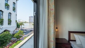 A hotel room with a view of a city street, a bed, a nightstand, and a window with curtains. - Danapearl Riverside Condotel (Da Nang)