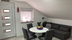 A dining area with a round table, four chairs, a gray sofa, and a window with blinds. - App. 80 meters from the sea (Vir)