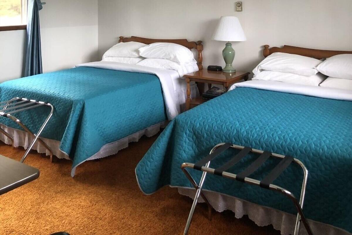 Une chambre d’hôtel avec deux lits, une fenêtre avec des rideaux, une lampe et deux tableaux au mur.