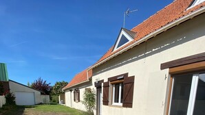 A residential property with a paved driveway, a lawn, and a house with a tiled roof and wooden shutters.