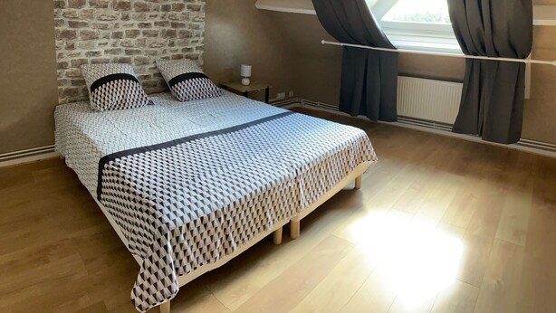 A bedroom with a brick wall, a bed with patterned bedding, a nightstand, and a window with curtains.