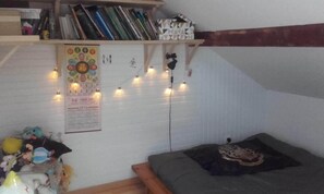 Um quarto aconchegante com uma cama, uma estante de livros, um cartaz e luzes de fada.