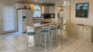 A kitchen with a central island, white bar stools, a refrigerator, and a microwave. - Vintage Vero Bungalow (Vero Beach)