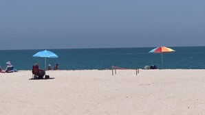 A beach with two umbrellas, a person in a chair, and a clear view of the ocean. - Vintage Vero Bungalow (Vero Beach)