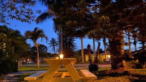 A wooden picnic table in a grassy area with palm trees and houses in the background. - Vintage Vero Bungalow (Vero Beach)