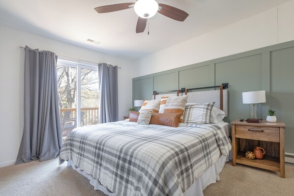 Une chambre avec un lit, une table de chevet, un ventilateur de plafond et une vue sur l’extérieur.