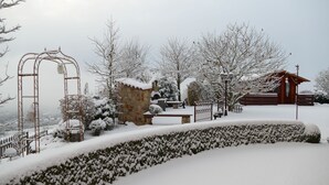 Een sneeuwbedekte tuin met een stenen constructie, een metalen toegangspoort en houten banken.