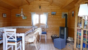 Een gezellig interieur van een chalet met een houten eettafel, stoelen, een bank, een open haard en een boekenkast.