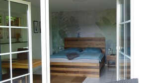 Een slaapkamer met een houten bed, een nachtkastje en een groot raam.