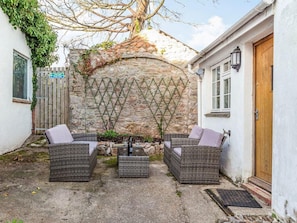 Relax in a serene outdoor seating area with wicker sofas and a small table, set against a stone wall with a lattice design.