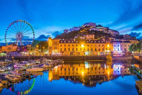 Enjoy waterfront views of a marina with a Ferris wheel and a hilltop complex featuring a mix of architectural styles.